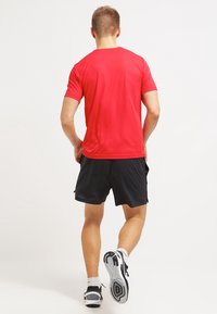 Czerwona koszulka sportowa z krótkim rękawem w zestawie z czarnymi szortami. Koszulka ma gładką teksturę, podczas gdy szorty są lekkie i luźne.