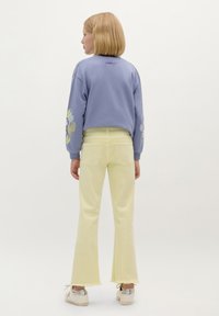 Felpa lavanda corta con ricami floreali sulle maniche; abbinata a jeans giallo chiaro a zampa d'elefante e sneakers bianche con dettagli argentati.