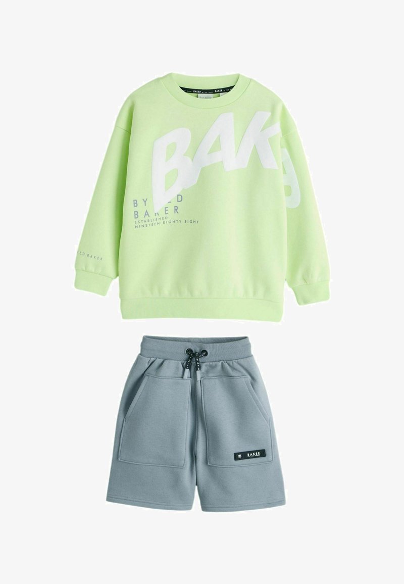 Lysegrøn sweatshirt med store hvide bogstaver og blå detaljer, kombineret med grå shorts med lommer og snøre i taljen.