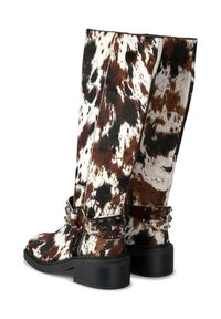 Botas altas con un patrón de piel de vaca en marrón, negro y blanco, que presentan correas de cuero con tachuelas y tacones bajos en negro.