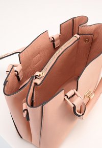 Torebka strukturalna w kolorze brzoskwiniowym z teksturowanym wykończeniem, czarnymi wykończeniami, złotym zamkiem błyskawicznym i dwoma komorami wewnętrznymi. Posiada górną rączkę i klipsy.