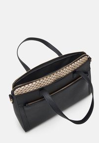 Sac fourre-tout en cuir noir avec fermetures éclair dorées, deux poignées et doublure en tissu beige à motifs visible à l'intérieur du compartiment supérieur ouvert.