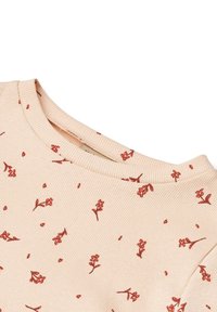 Bézs bordázott anyagból készült felső, apró, szórtan elhelyezkedő piros virágmintával és kerek nyakkivágással.