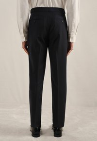 Pantaloni negri uni, cu croială dreptă, având două buzunare la spate și o textură a materialului neted, asortați cu pantofi negri.