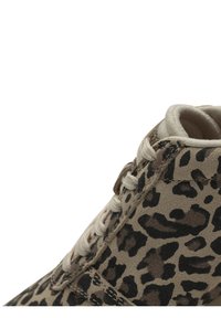 Chaussure en daim à imprimé léopard dans des tons beige et marron, avec des lacets blancs et un bout arrondi. Surface texturée avec un motif animal prononcé.