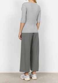 Szary, prążkowany, dopasowany top z rękawami do łokcia, w połączeniu z luźnymi, ciemnoszarymi spodniami typu wide-leg. Uzupełniony jasnymi butami sportowymi.