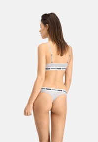Szary zestaw bielizny składający się z stanika typu bralette z regulowanymi ramiączkami oraz pasującego stringów. Oba elementy mają czarną, markową tasiemkę w talii.