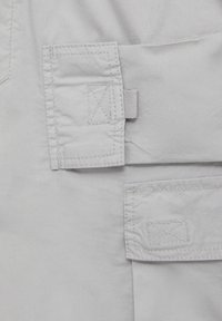 Gros plan sur un tissu gris clair avec deux poches rectangulaires cousues, chacune munie d'une boucle de languette cousue sur le côté.