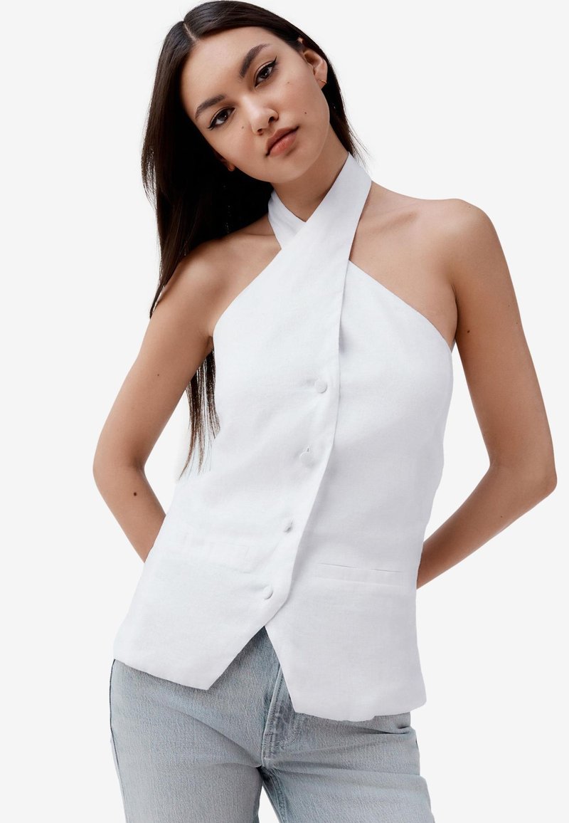 Fehér lenpántos topp átfedő dizájnnal, gombzárral és testre szabott szabással, világoskék farmernadrággal párosítva.