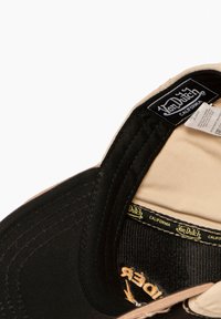 Gorra negra y marrón con visera curvada. El interior presenta una etiqueta y costuras en contraste. Superficies texturizadas y correa ajustable visibles.