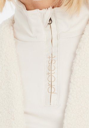 Gros plan sur une veste en polaire blanche avec un col zippé et un texte beige "protest" sur la patte de fermeture éclair.