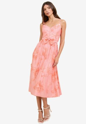 Pink floral-printed dress with spaghetti straps, a fitted bodice, and a bow accent at the waist. Flowy skirt reaches mid-calf.