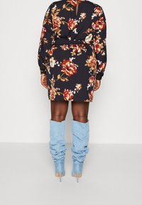 Květinové šaty s dlouhými rukávy, námořnická modř jako základ a živé červené, žluté a bílé květiny. Vybaveno stylovými světle modrými botami s nařasením.