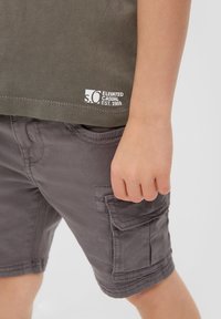 Grijze cargoshorts met zijzakken en gestikte accenten, gecombineerd met een groene t-shirt met een wit logo en strakke lijnen.