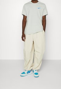 Light gray cotton t-shirt with a small blue logo, paired with cream-colored wide-leg pants and blue and purple sneakers.