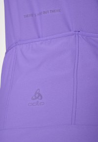 T-shirt de sport violet avec un tissu texturé, un design sans couture et un branding discret. La phrase "IL Y A PLUS LÀ DEHORS" est visible au-dessus.