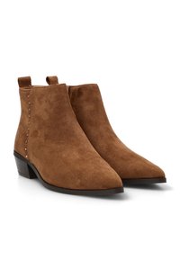 Botines de ante marrón con punta afilada, tacón bajo y cuadrado, y tachuelas decorativas a lo largo del lado. Tobillo elástico para facilitar su uso.