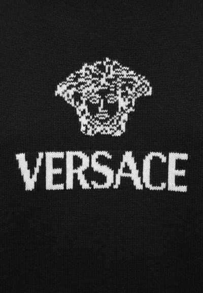 Černá pletená látka s bílým logem hlavy Medúzy nad textem „VERSACE“ tučnými velkými písmeny. Design je monochromatický.