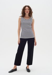 Top a righe senza maniche in blu navy e bianco, abbinato a pantaloni neri a gamba larga e scarpe nere flat, su uno sfondo bianco uniforme.
