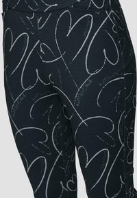 Zwarte legging met een hartpatroon in het wit. Zachte, rekbare stof met een aansluitend ontwerp en subtiele tekstaccenten door het geheel.