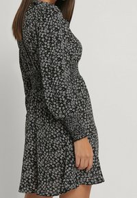 Vestido negro con estampado de flores blancas pequeñas, con cintura fruncida, mangas largas abullonadas y falda acampanada. Fabricado con tejido ligero.