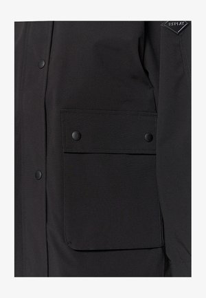 Schwarze Jacke mit einer vorderen Tasche mit Klappe und Druckknöpfen, aus strukturiertem Stoff gefertigt, zeigt ein elegantes, minimalistisches Design.