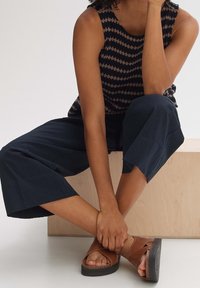 Pantalon court bleu marine en tissu texturé, associé à un top sans manches à motif en zigzag de couleurs foncées et claires, et des sandales marron.