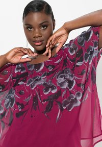 Luftig, transparent maroon bluse med sort blomsterprint og sølvpynt. Har en bred, scoop-neck og løse ærmer.