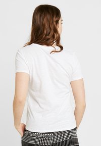 Camiseta blanca de manga corta con cuello redondo, hecha de tejido ligero; textura suave, con un diseño sencillo sin patrones.