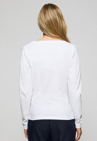 Camicetta bianca a maniche lunghe con scollatura quadrata. Tessuto morbido, superficie liscia e design aderente. Retro pulito, abbinata a pantaloni scuri.