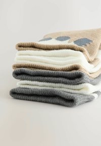 Pile de quatre couvertures en tricot beige, blanche et grise. Texture douce avec un motif bleu clair sur la couverture du dessus.