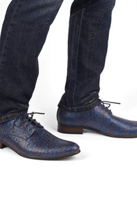 Donkerblauwe gepatternde schoenen met een textuur, ronde neus en vetersluiting, gecombineerd met donkere spijkerbroek.