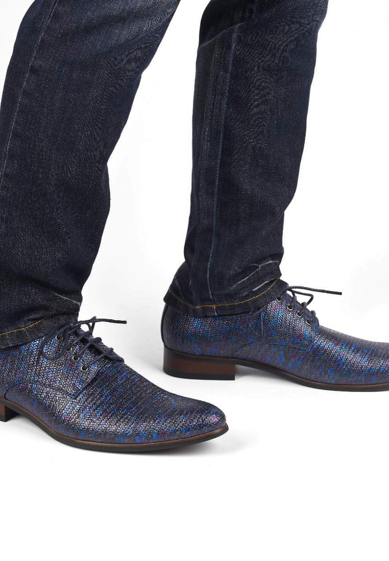 Donkerblauwe gepatternde schoenen met een textuur, ronde neus en vetersluiting, gecombineerd met donkere spijkerbroek.