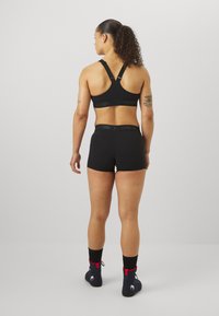 Μαύρο αθλητικό σουτιέν με ρυθμιζόμενες τιράντες, σε συνδυασμό με μαύρες σορτσάτες παντελόνες ψηλής μέσης. Το υλικό φαίνεται ελαστικό και διαθέτει λάστιχο με λογότυπο στη μέση.