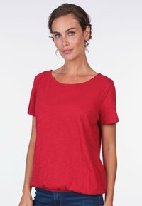 Red, short-sleeve T-shirt made of soft, lightweight fabric with a round neckline and a relaxed fit, featuring a gathered hem detail.