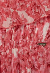 Różowa kwiatowa sukienka plisowana z przejrzystą teksturą, falbaniastymi warstwami i metalową metką marki. Wzór na tkaninie składa się z delikatnych, różowych motywów.