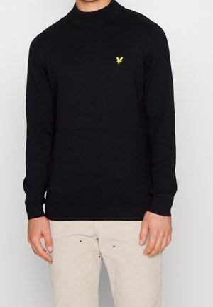 Zwarte trui met een hoge hals en lange mouwen. Voorzien van een klein geel logo op de borst. De stof lijkt zacht en gebreid te zijn.