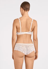 Soutien-gorge en dentelle blanche et culotte assortie, avec des motifs floraux, des bords festonnés et des accents de boutons au dos. Bretelles ajustables.