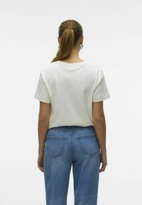 Camiseta blanca de algodón con mangas cortas y cuello redondo, combinada con jeans de mezclilla azules con bolsillos traseros y un corte holgado.