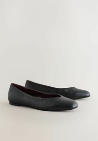 Czarne skórzane baletki z zaokrąglonym noskiem i niskim obcasem. Wnętrze ma kontrastową bordo podszewkę i bezszwowy design.