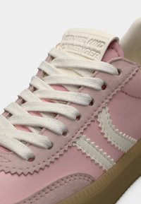 Ροζ αθλητικό παπούτσι με δέρμα με υφή, λευκές ραφές, επίπεδα κορδόνια και ετικέτα γλώσσας σε κρεμ απόχρωση. Σόλα από καουτσούκ με ζιγκ-ζαγκ σχεδίαση.