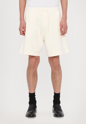 Cream-colored, mid-length shorts with an elastic drawstring waistband and side pockets, made of soft, textured fabric.