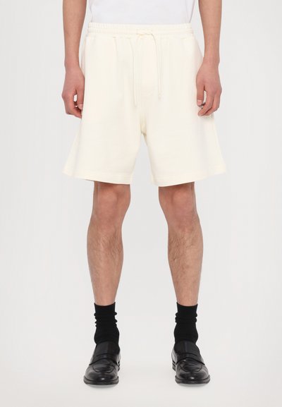 Shorts crème, de longueur mi-genoux, avec une taille élastique à cordon de serrage et des poches latérales, fabriqués dans un tissu doux et texturé.
