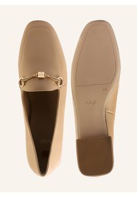 Beige leather loafers with a square toe, featuring a gold chain accent. The flat sole has textured grip and branding on the insole.