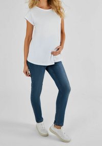 Biała koszulka z krótkim rękawem w luźnym kroju, zestawiona z dżinsami o średnim odcieniu i dopasowanym kroju oraz białymi trampkami, prezentująca swobodny wygląd.