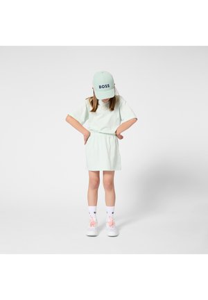 Vestido tipo camiseta de color verde menta con cintura elástica y detalle de logo. Combina con una gorra a juego, calcetines blancos y zapatillas de color rosa pastel.