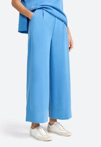 Pantaloni sportivi larghi di colore azzurro chiaro realizzati in tessuto morbido, con tasche laterali e orlo piegato, abbinati a sneakers bianche.