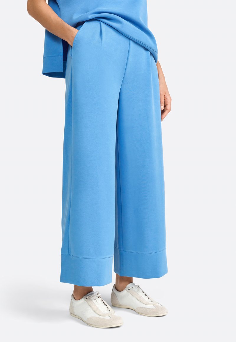 Pantaloni sportivi larghi di colore azzurro chiaro realizzati in tessuto morbido, con tasche laterali e orlo piegato, abbinati a sneakers bianche.