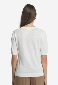 Hvid let strikket sweater med korte ærmer, ribbet kant og blød tekstur. Enkelt design med rund hals og uden synlige mønstre.