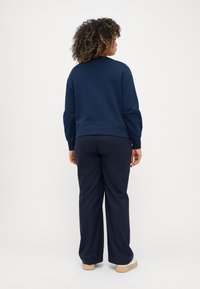 Mørkeblå hettegenser og matchende bukser i et mykt stoff. Hettegenseren har ribbestrikket kant og mansjetter, med en avslappet passform. Flate sko fullfører antrekket.